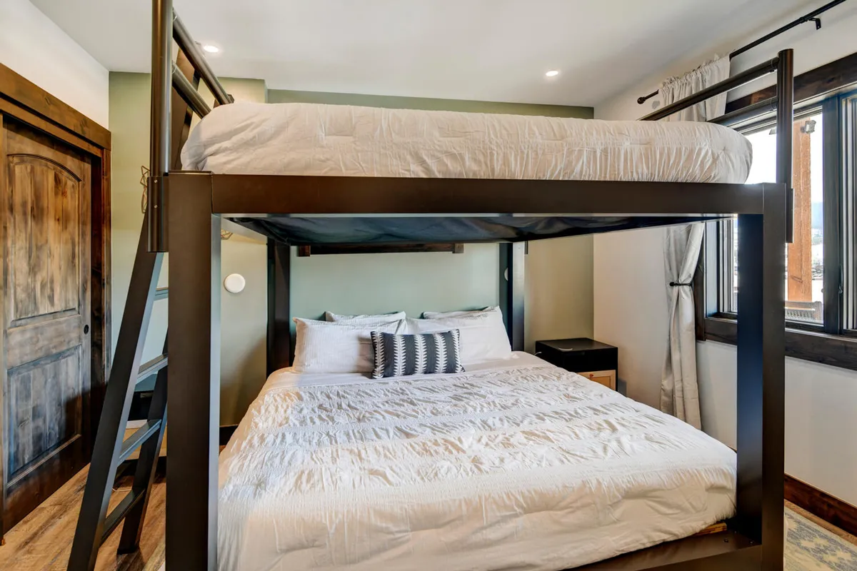 A stylish bunk room equipped with king-over-king bunk beds, decorated with playful pillows and accented by natural light from large windows. The space is lively, inviting, and ideal for kids, teens, or friends seeking a cozy and fun retreat.