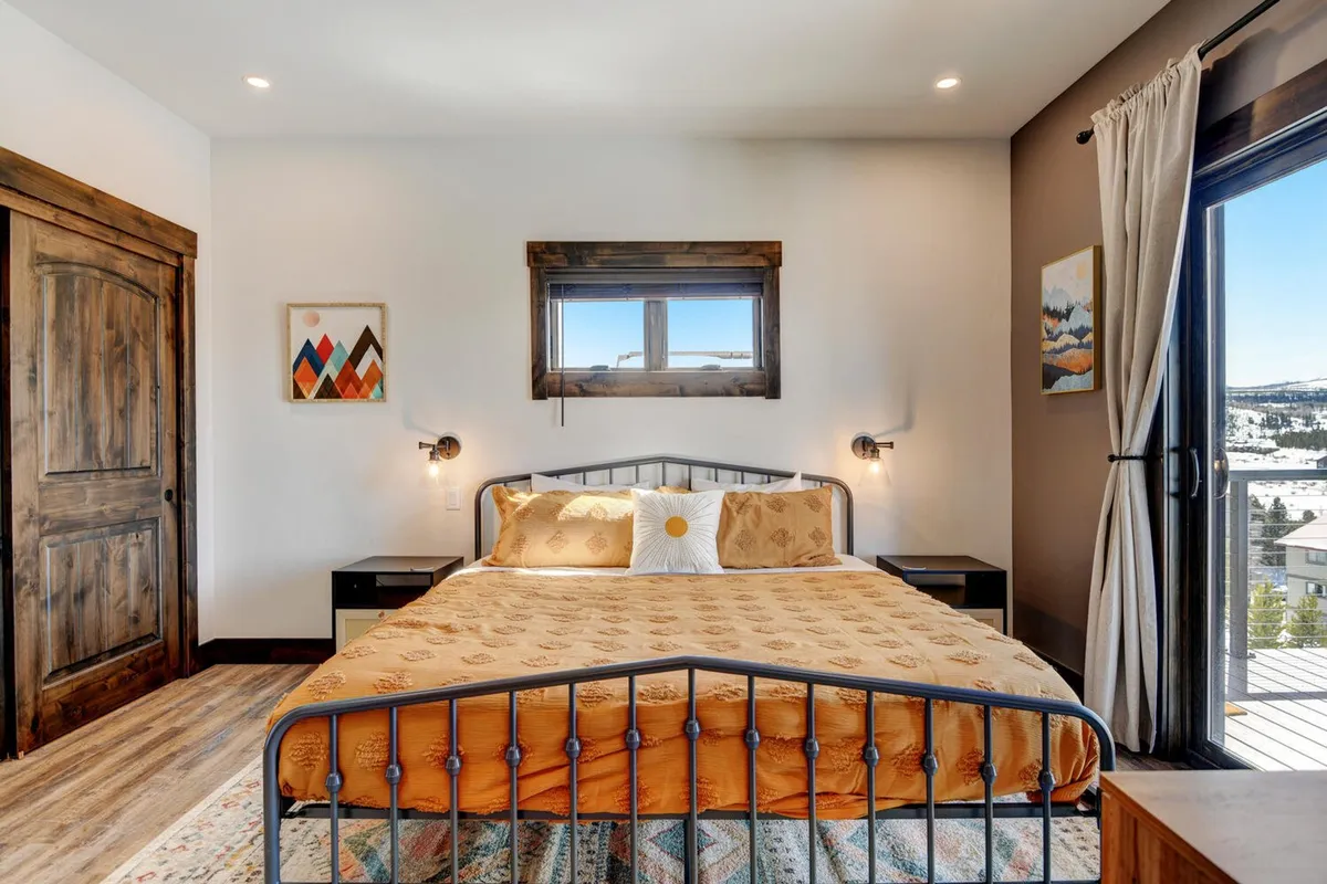 A comfortable bedroom with patterned bedding, decorative pillows, and artwork, illuminated by natural light coming through a window with a scenic view. The mood is restful and welcoming—ideal for lazy mornings or peaceful evenings.