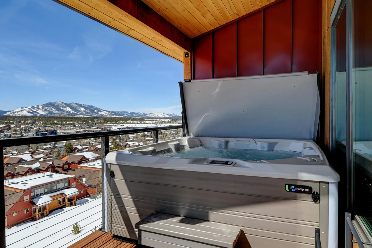 A tranquil exterior scene featuring a private hot tub set on a balcony or deck, with comfortable seating and a panoramic mountain view. People are seen relaxing in the hot tub, socializing, and enjoying the sunset, conveying a sense of luxury and relaxation in a natural setting.