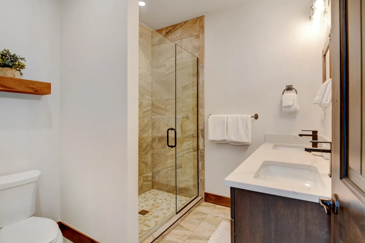 A modern bathroom featuring a glass walk-in shower, double sinks, and a decorative shelf. The design is clean and tranquil, with ample space for personal grooming and relaxation after a day of adventure.
