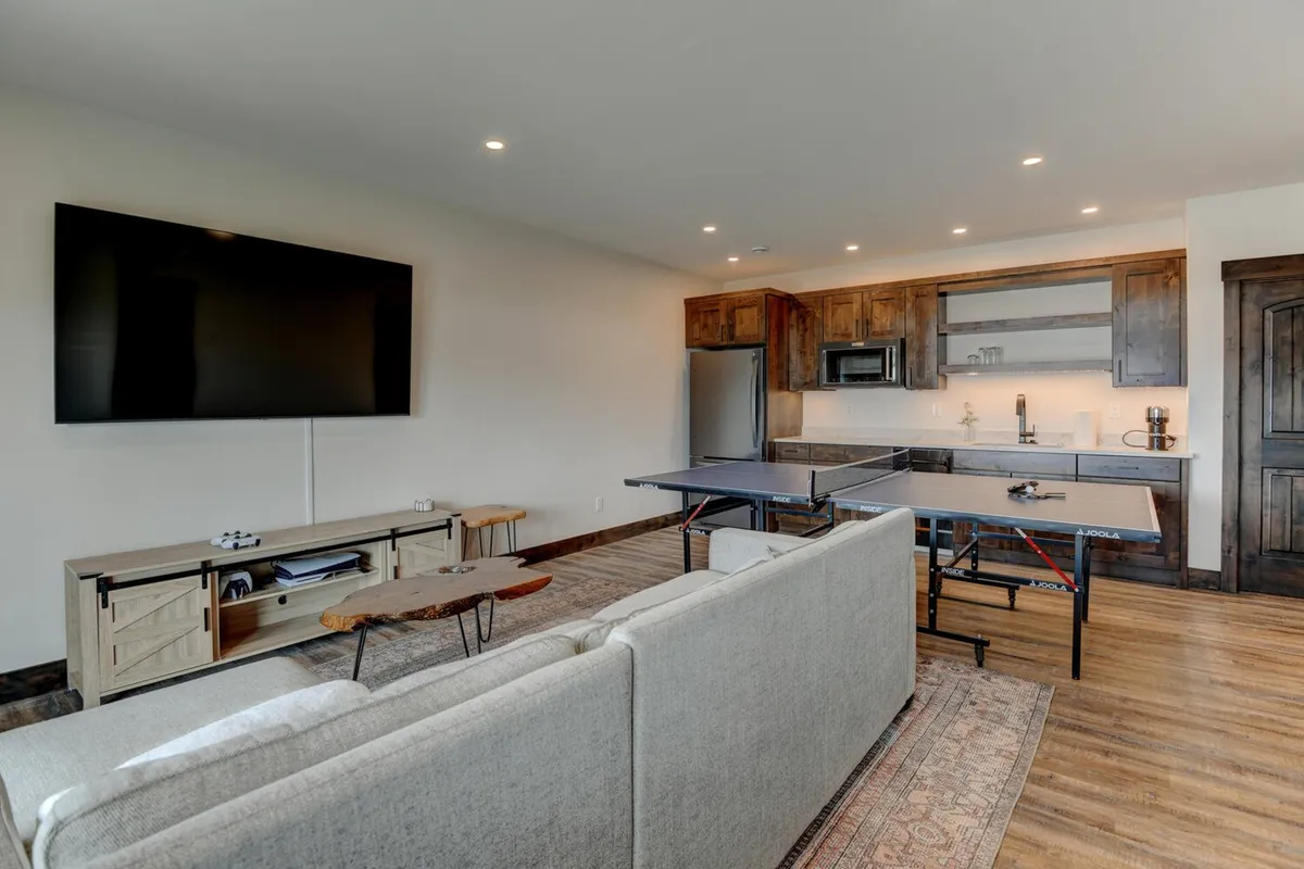 A flexible recreation space with a large TV perfect for movie nights, a ping pong table for friendly competition, a kitchenette area for snack prep, and a comfortable sofa for group lounging. The layout encourages all-ages fun and socializing.