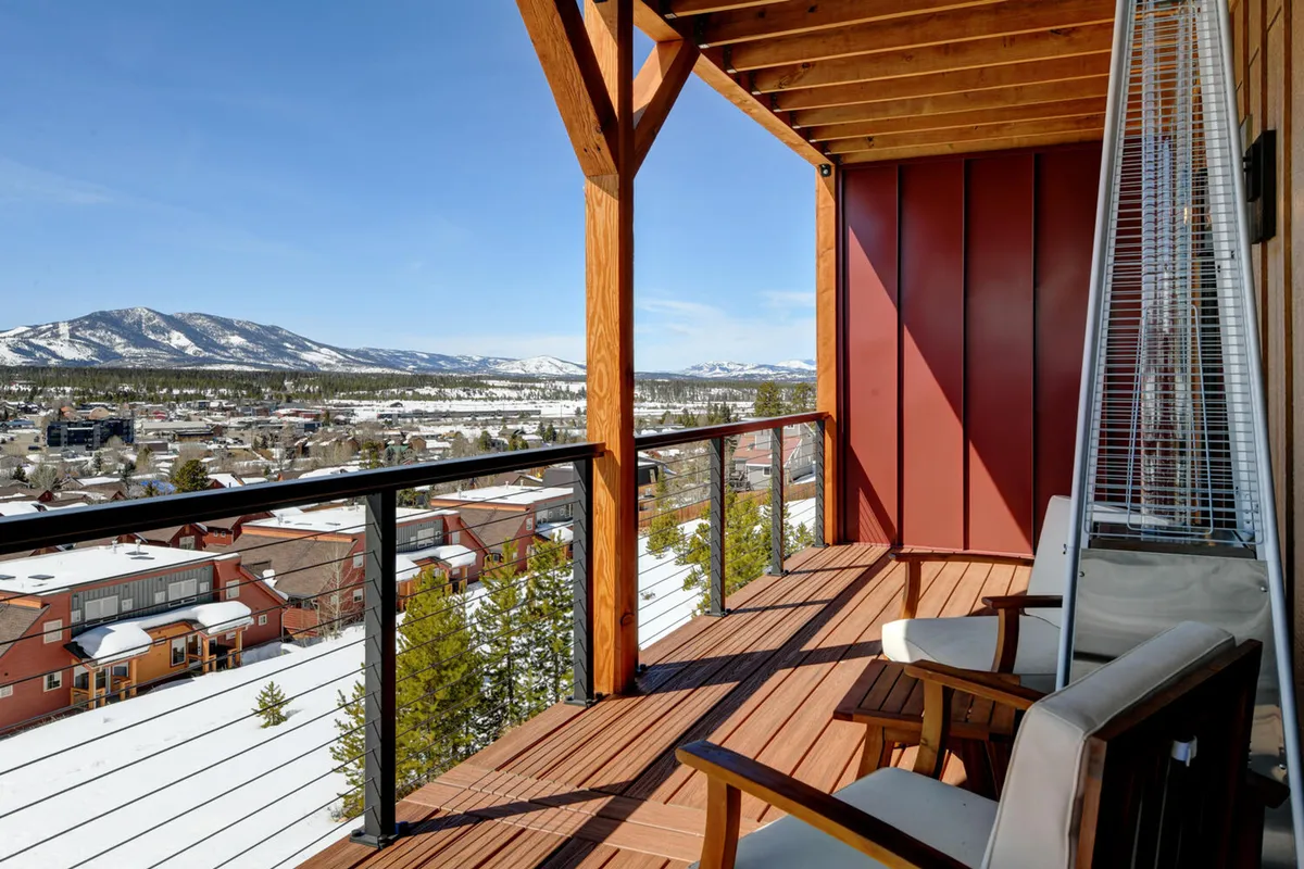 A serene wooden balcony overlooks a snow-covered landscape and sweeping mountain views. The space is open and inviting, ideal for lounging after a day outside, and exemplifies the connection between indoor comfort and outdoor adventure.