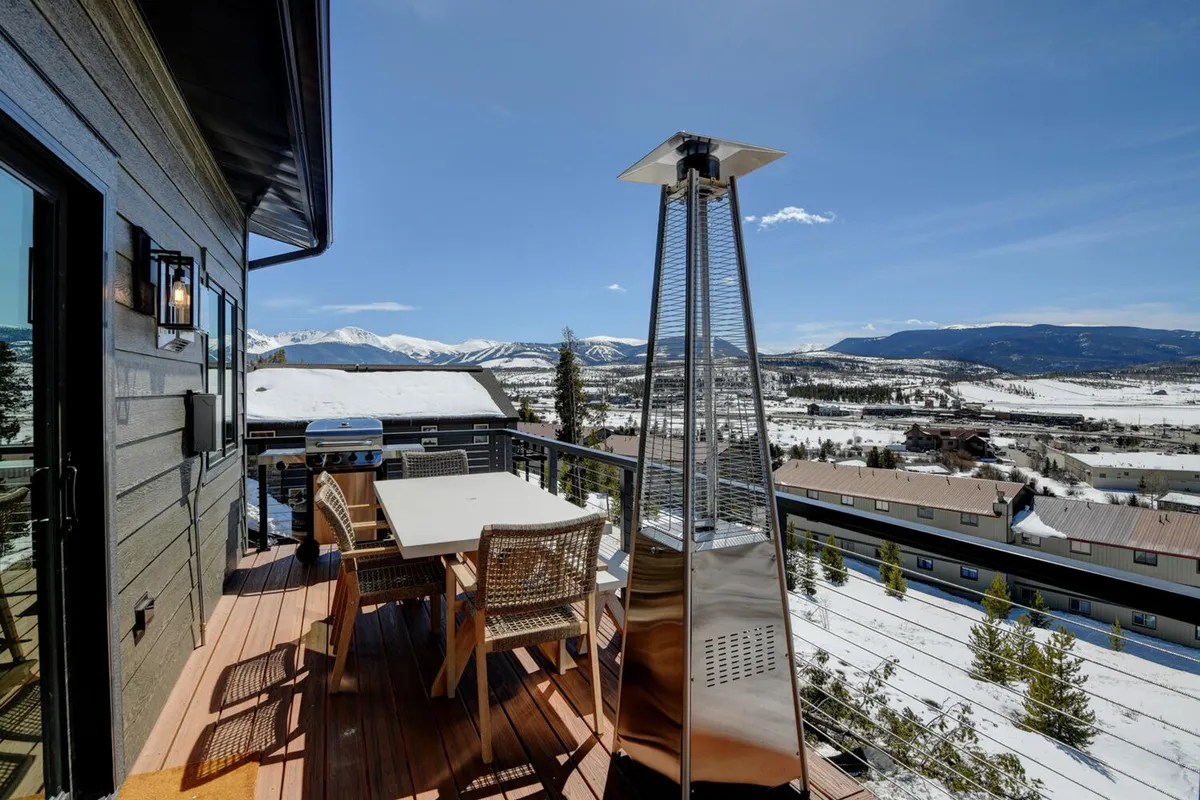 An exterior deck with a dining table and patio heater overlooks sweeping mountain vistas. The setup suggests al fresco meals, sunset gatherings, or morning coffee in the crisp alpine air, all surrounded by natural beauty.