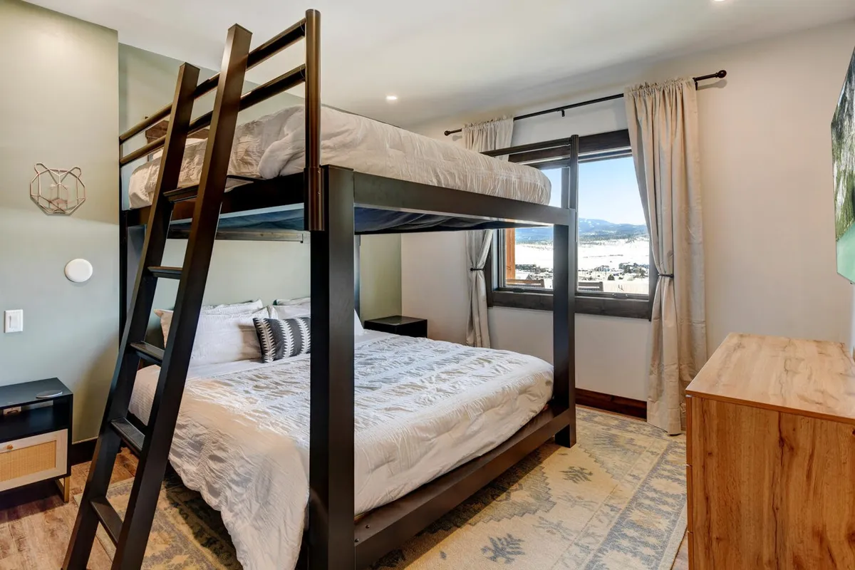 A playful yet comfortable bunk bed room with a window view and a decorative rug, designed for family bonding or group sleeping. The space feels fun and flexible, catering to children, teens, or adults in need of extra sleeping arrangements.